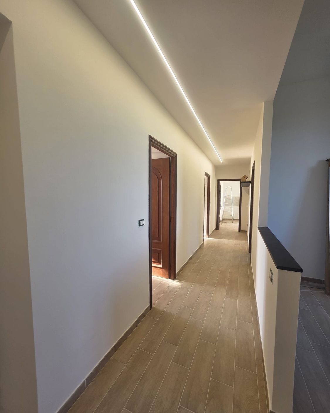 Lo stesso corridoio finito, con la striscia LED nel soffitto e il pavimento effetto legno